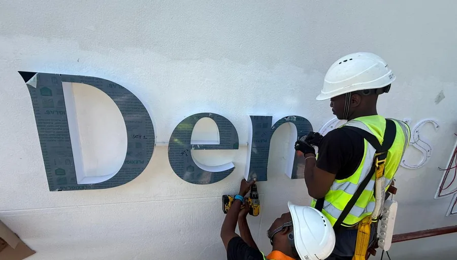 Umhlanga Signs installers in PPE fitting fabricated channel letters to a building facade