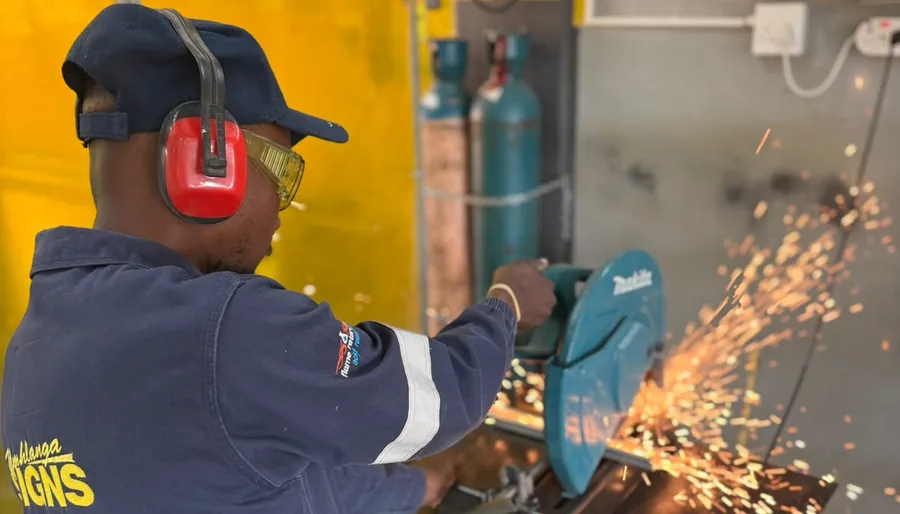 Umhlanga Signs fabricator cutting steel section on a chop saw in the Glen Anil workshop